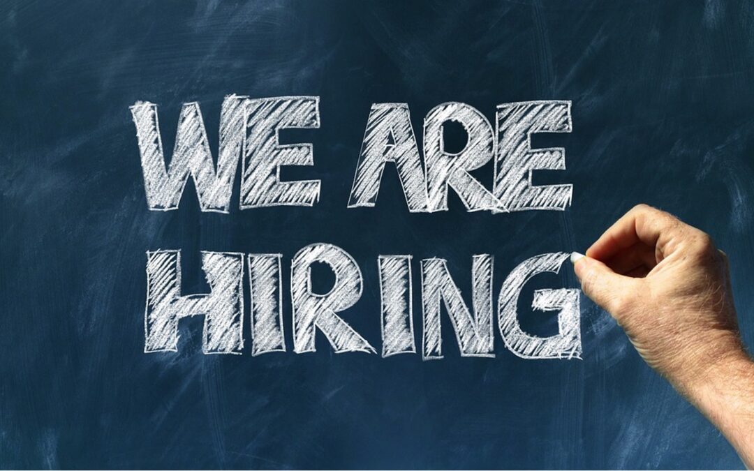 A hand writing the word "we are hiring" on a blackboard serves as a guide for potential applicants in 2024.